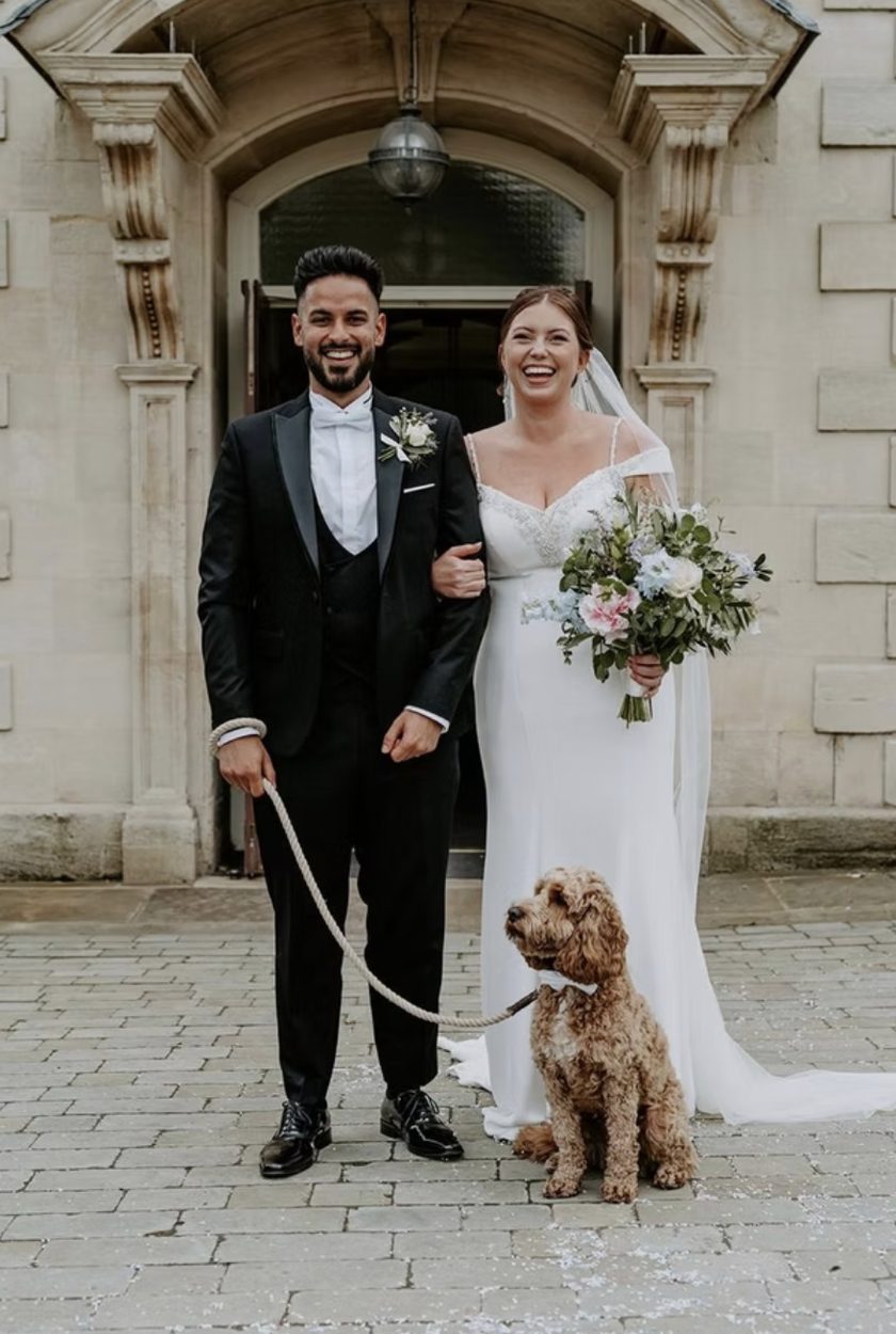 Bride, groom and their dog outside a stone manor